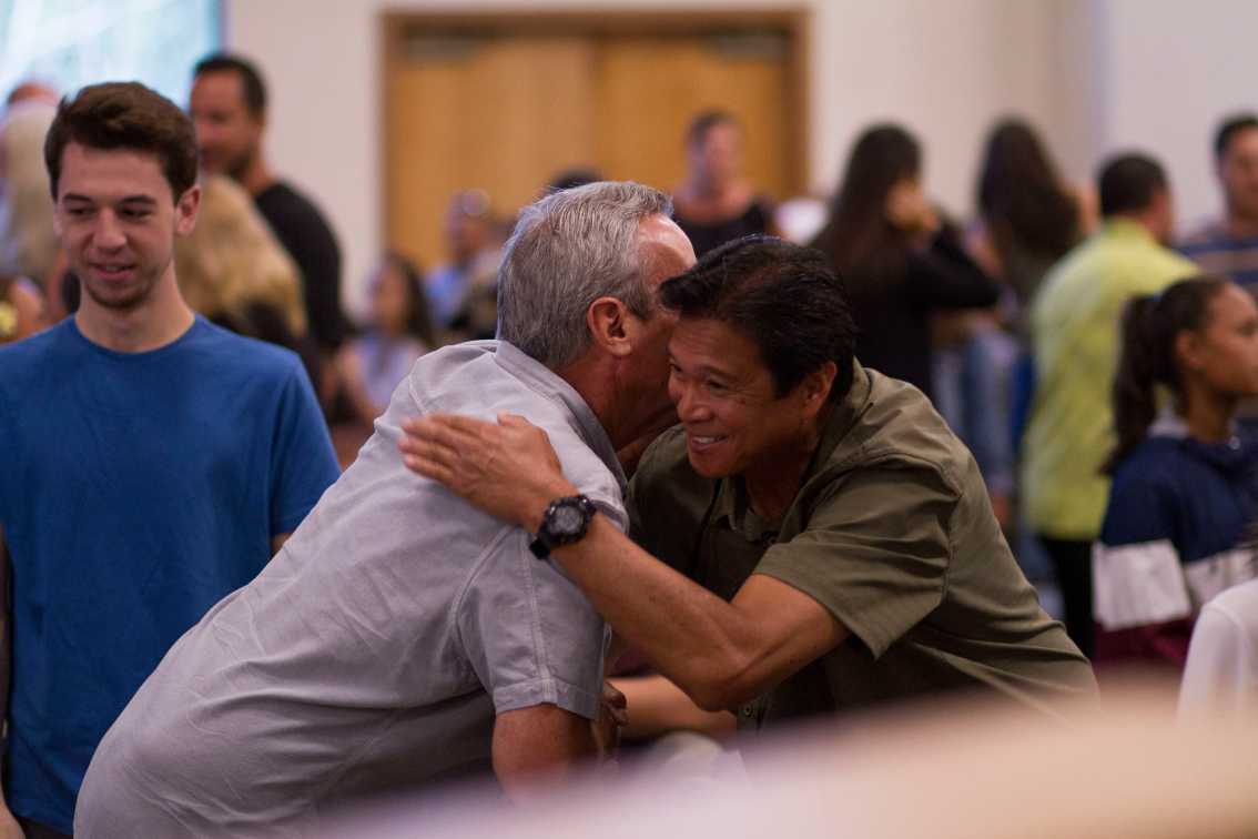Two men hugging in a room full of people